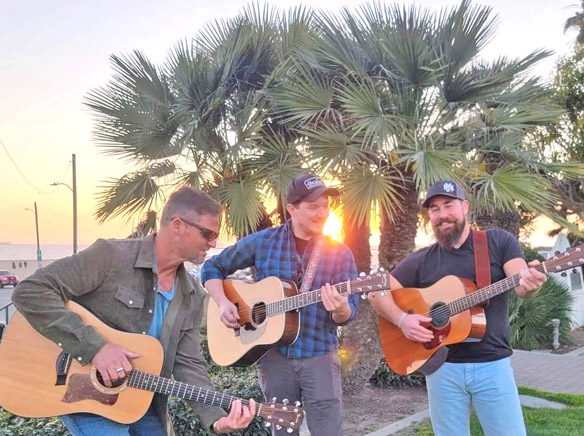 Three country western singer with guitars singing with the beach in the background